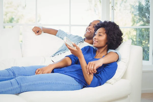 Lyckligt par liggande på soffan håller fjärrkontrollen — Stockfoto