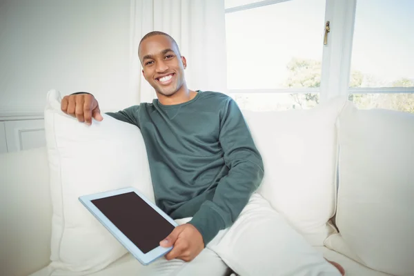 Hombre sonriente sosteniendo la tableta en el sofá —  Fotos de Stock