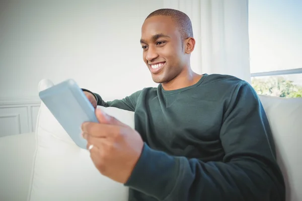 Homme souriant tenant la tablette sur le canapé — Photo