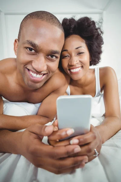 Smiling couple using smartphone on bed — Stock Photo, Image