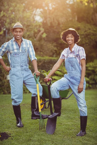 Smiling couple holding shovel and rake — Stockfoto