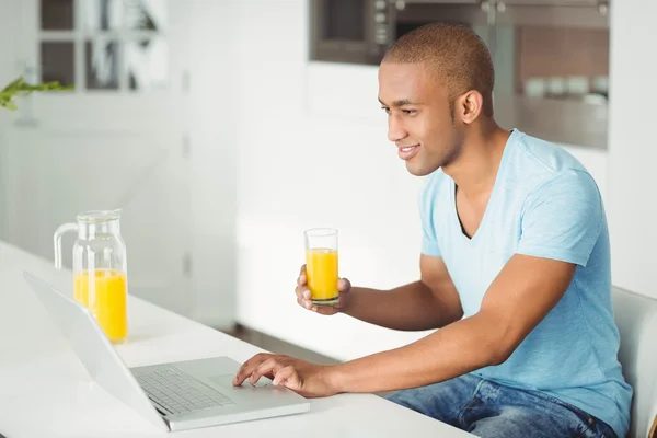 Homme utilisant un ordinateur portable et boire du jus d'orange — Photo