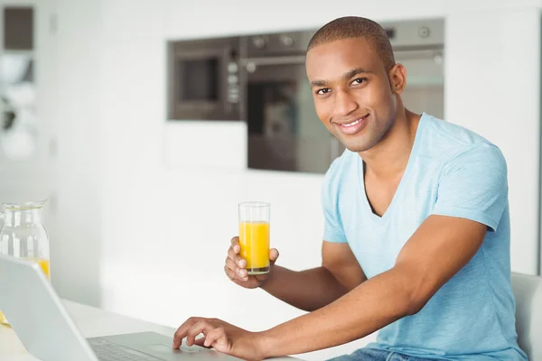 Homem usando laptop e beber suco de laranja — Fotografia de Stock