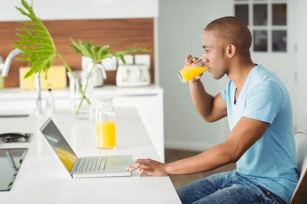 Homem usando laptop e beber suco de laranja — Fotografia de Stock