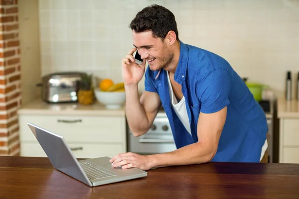 Young man using laptop and talking on phone — Stock Fotó