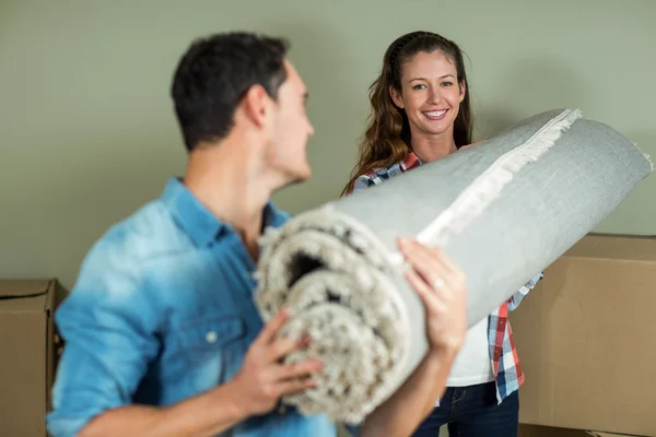 Happy couple carrying rolled up rug — Stock Photo, Image