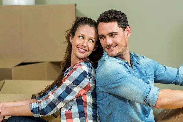 Pareja joven sentada espalda con espalda en su nueva casa — Foto de Stock