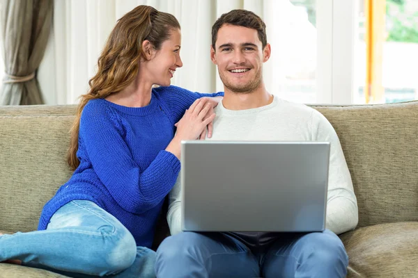 Casal jovem sorrindo cara a cara no sofá e usando laptop — Fotografia de Stock