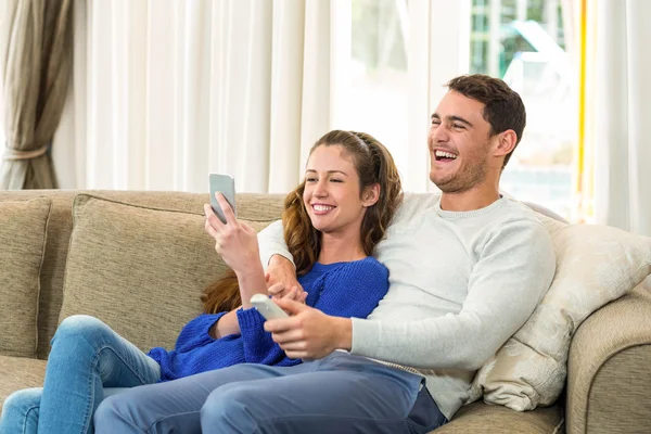 Jovem casal sentado no sofá e usando telefone celular — Fotografia de Stock