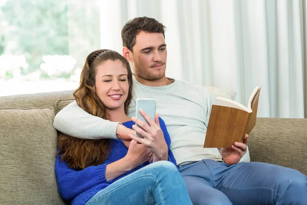 Jovem casal sentado no sofá e usando telefone celular — Fotografia de Stock