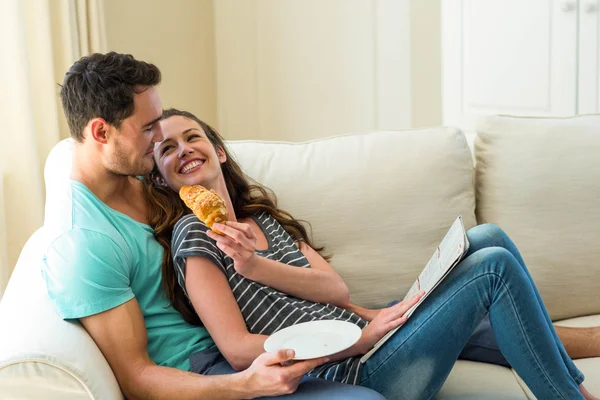 Pareja joven tomando croissant mientras lee el periódico — Foto de Stock