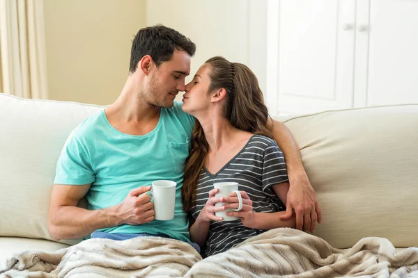 Pareja joven abrazándose en el sofá mientras toma café —  Fotos de Stock