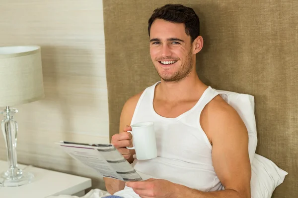 Young man reading newspaper while holding a cup of tea — ストック写真