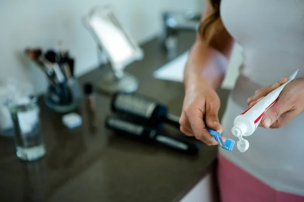 Woman squeezing toothpaste onto toothbrush — Stock Photo, Image