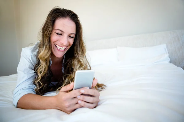 Žena leží na posteli na její mobilní telefon — Stock fotografie