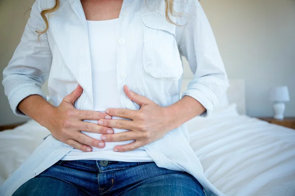 Woman sitting on her bed clutching her stomach — Stock Photo, Image