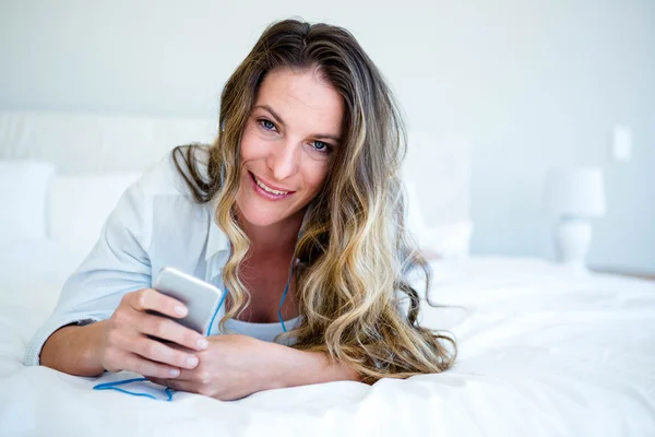 Lächelnde Frau, die auf ihrem Bett liegt und Musik hört — Stockfoto