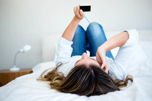 Vrouw liggend op haar bed luisteren naar muziek — Stockfoto
