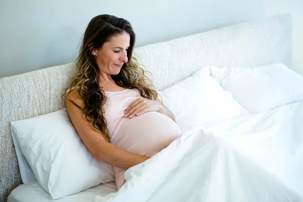 Zwangere vrouw in bed holding haar bump — Stockfoto