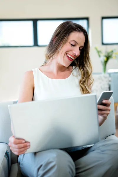 Mujer sonriente en su computadora portátil y teléfono móvil — Foto de Stock