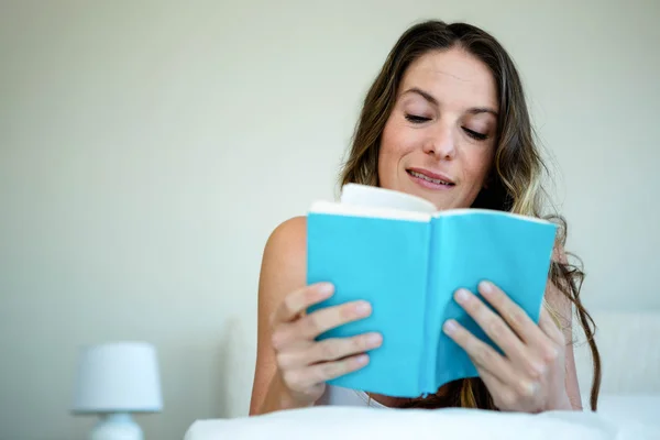 Lächelnde Frau beim Lesen eines Buches im Bett — Stockfoto