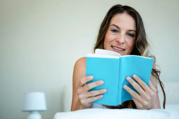 Mosolygó nő az ágyban, egy könyvet olvas — Stock Fotó
