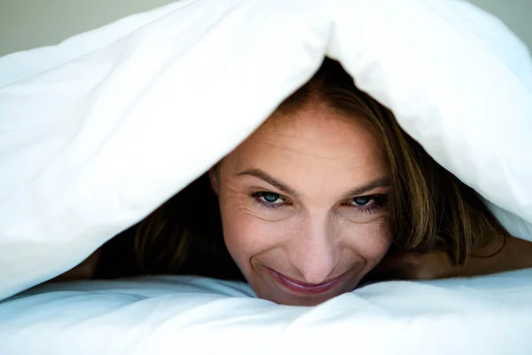 Woman peering out from under her duvet — Stock Photo, Image