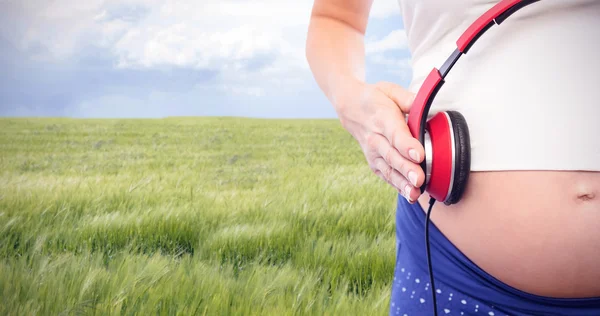 Pregnant woman holding earphones over bump — Stock Photo, Image