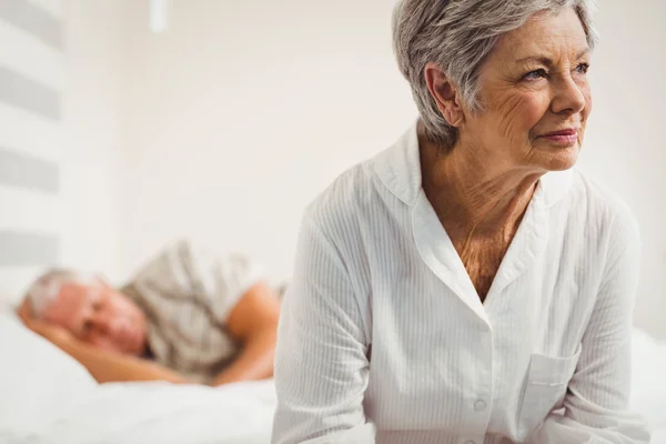 Preoccupata donna anziana seduta sul letto — Foto Stock