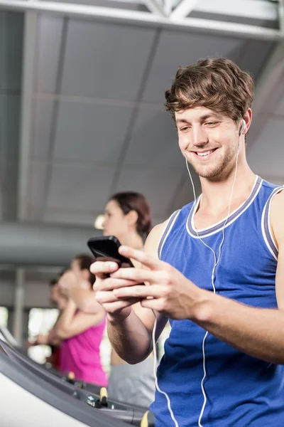 Lächelnder muskulöser Mann auf dem Laufband, der Musik hört — Stockfoto