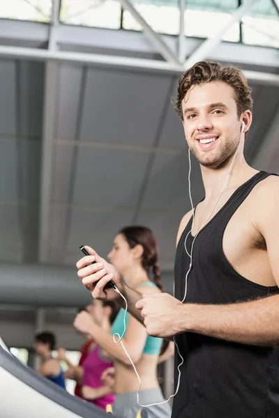 Lächelnder muskulöser Mann auf dem Laufband, der Musik hört — Stockfoto