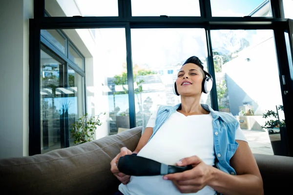 Zwangere vrouw luisteren naar muziek op de sofa — Stockfoto