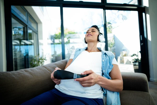 Terhes nő hallgathatja a zenét a kanapé — Stock Fotó