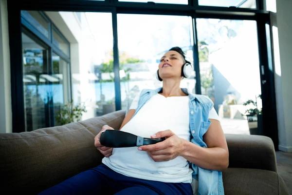 Femme enceinte écoutant de la musique sur le canapé — Photo