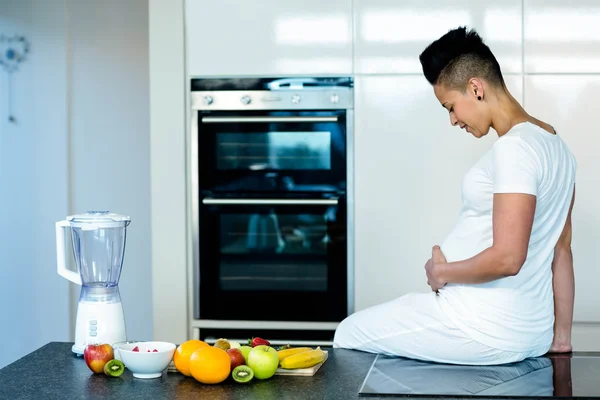 Femme enceinte assise sur le plan de travail de la cuisine — Photo