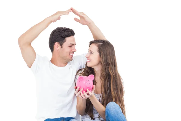 Young couple sitting on floor with piggy bank — Stock Photo, Image