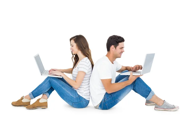 Happy couple sitting on the floor back to back using laptop — Stock Photo, Image