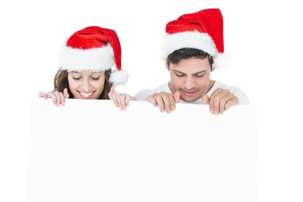 Glückliches Paar mit Weihnachtsmütze und einem Poster — Stockfoto