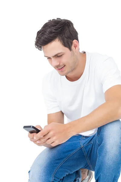 Handsome man crouching using a smartphone — Stock Photo, Image