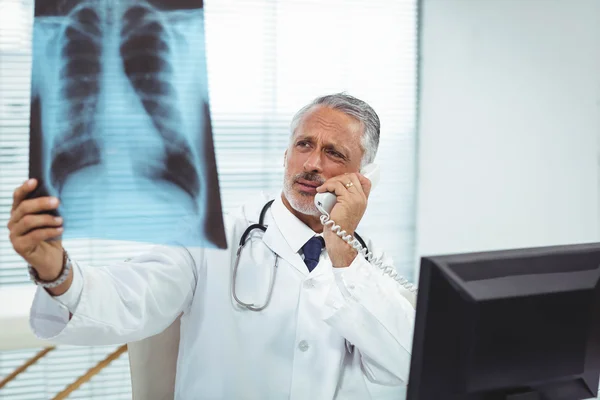 Médico revisando un informe de rayos X mientras habla por teléfono —  Fotos de Stock