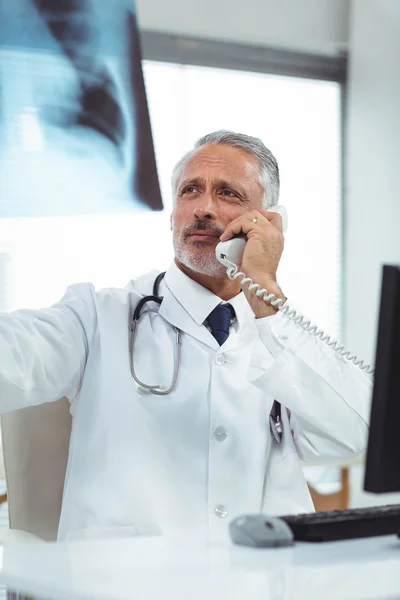 Médico revisando un informe de rayos X mientras habla por teléfono —  Fotos de Stock