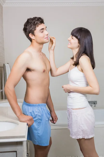 Vrouw toepassing moisturizer over mans gezicht — Stockfoto
