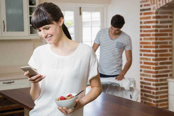 Kobieta przy użyciu telefonu komórkowego jedząc płatki śniadaniowe — Zdjęcie stockowe