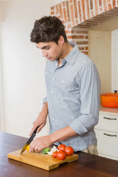 Молодой человек режет овощи на кухне — стоковое фото