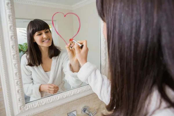 Young beautiful woman drawing big heart on mirror — Stock Photo, Image