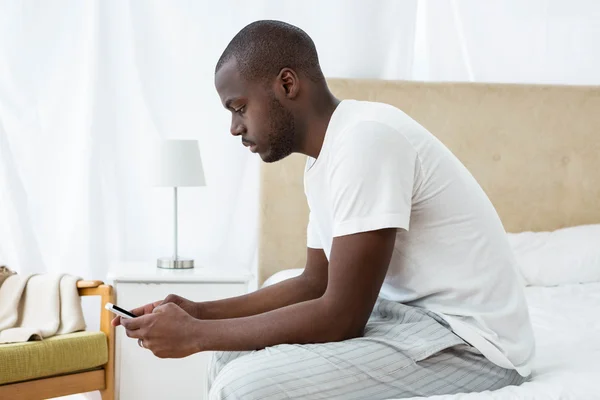 Man text messaging on mobile phone in bedroom — Stock Photo, Image