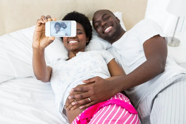 Casal feliz tocando barriga grávida tomando selfie — Fotografia de Stock