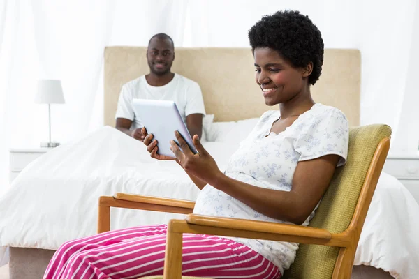 Pregnant woman using digital tablet on chair and man sitting on — Stock Photo, Image