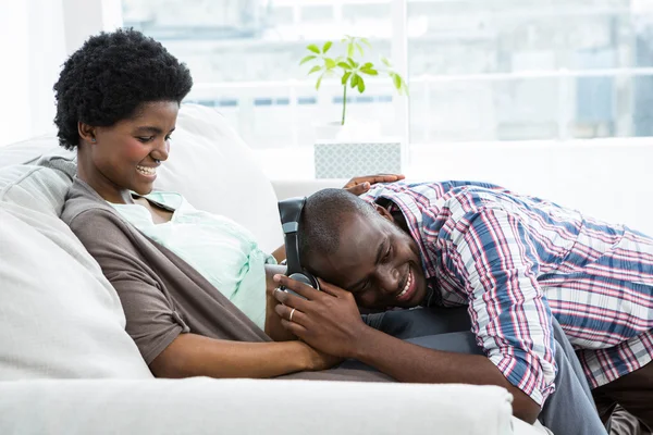 Man met hoofdtelefoon op dames maag — Stockfoto