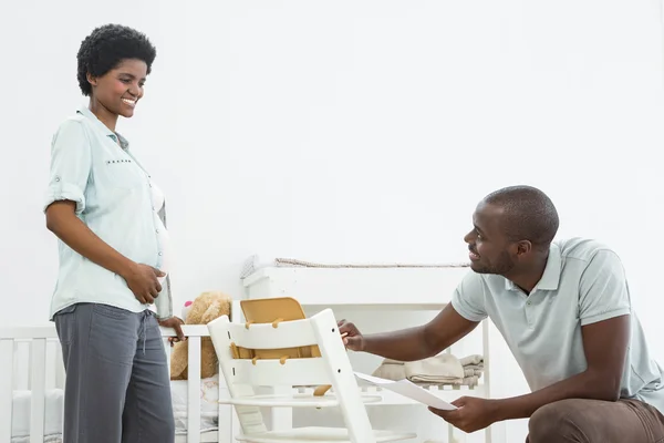 Mujer embarazada mirando al hombre arreglando una silla de bebé — Foto de Stock